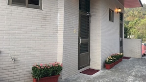 A building with a white brick exterior, a metal door with a security screen, and two potted plants with pink flowers. - Cheng Lan Hotel (Yuchi)