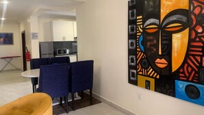 A modern hotel room with a dining area, a kitchen, and a large abstract painting on the wall. - Tennys Place Apartments GARKI (Abuja)