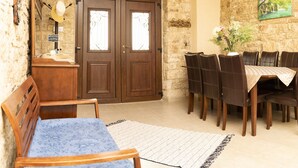 A room with a wooden bench, a dining table with chairs, a stone wall, and a door with a 'Welcome Home' sign.