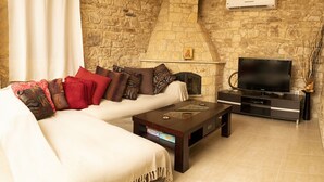 A living room with a stone wall, a fireplace, a sofa with cushions, a coffee table, and a TV.