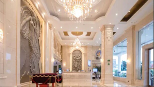 Un lobby majestuoso con una gran araña, columnas de mármol y una estatua.