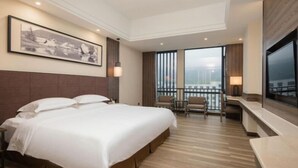 Habitación de hotel con una cama grande, un escritorio, una silla, un televisor y un balcón con vistas.
