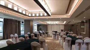 Un salón de conferencias con filas de sillas blancas, una mesa larga y un techo alto con iluminación empotrada.