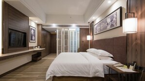 Habitación de hotel con una cama grande, un televisor de pantalla plana en la pared, una mesita de noche con lámpara y suelo de madera.