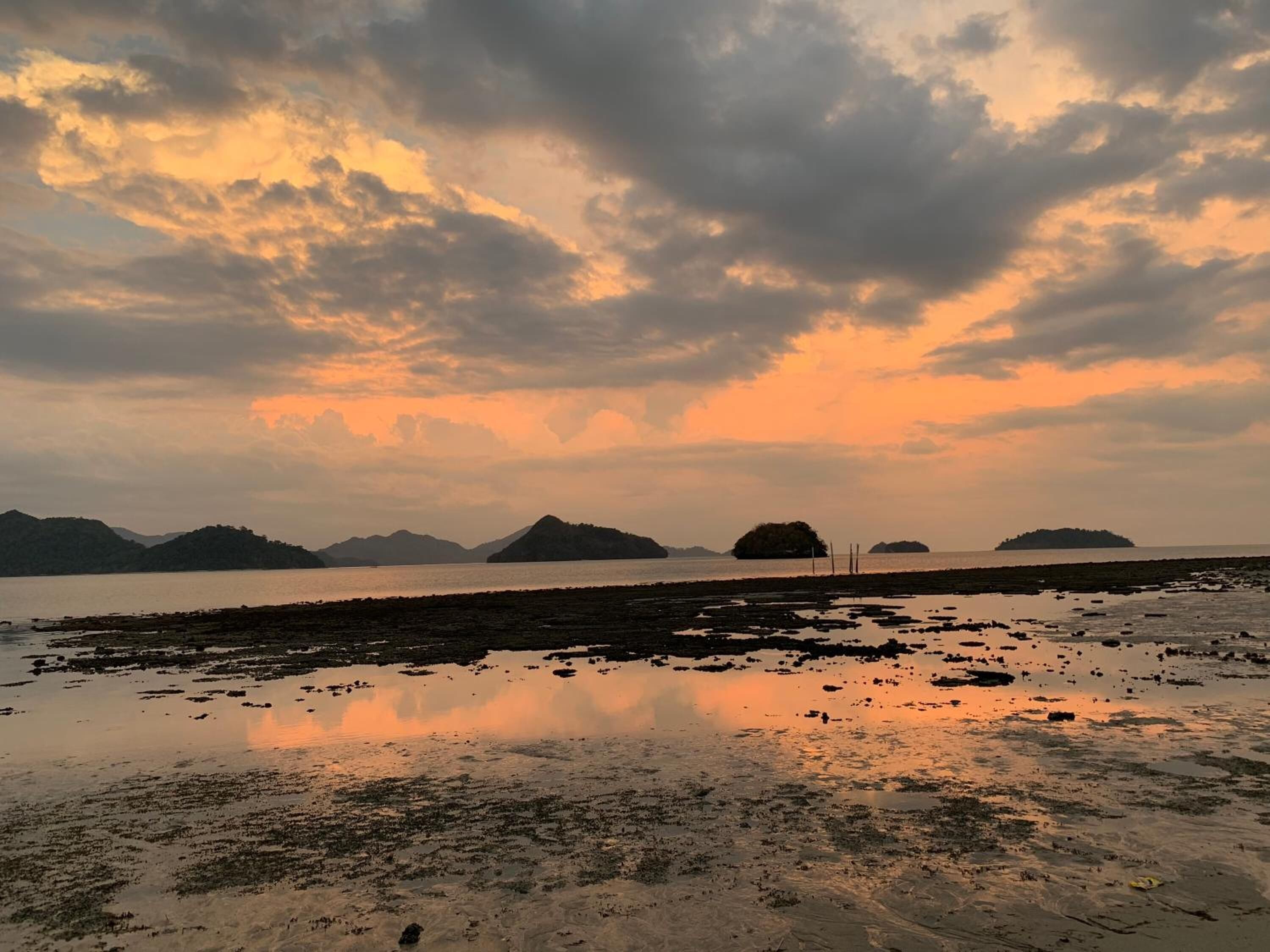 A coastal landscape with a calm sea, distant islands, and a cloudy sky.