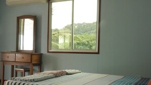 Une chambre à coucher avec un lit, une commode en bois, un miroir et une fenêtre donnant sur un paysage verdoyant.