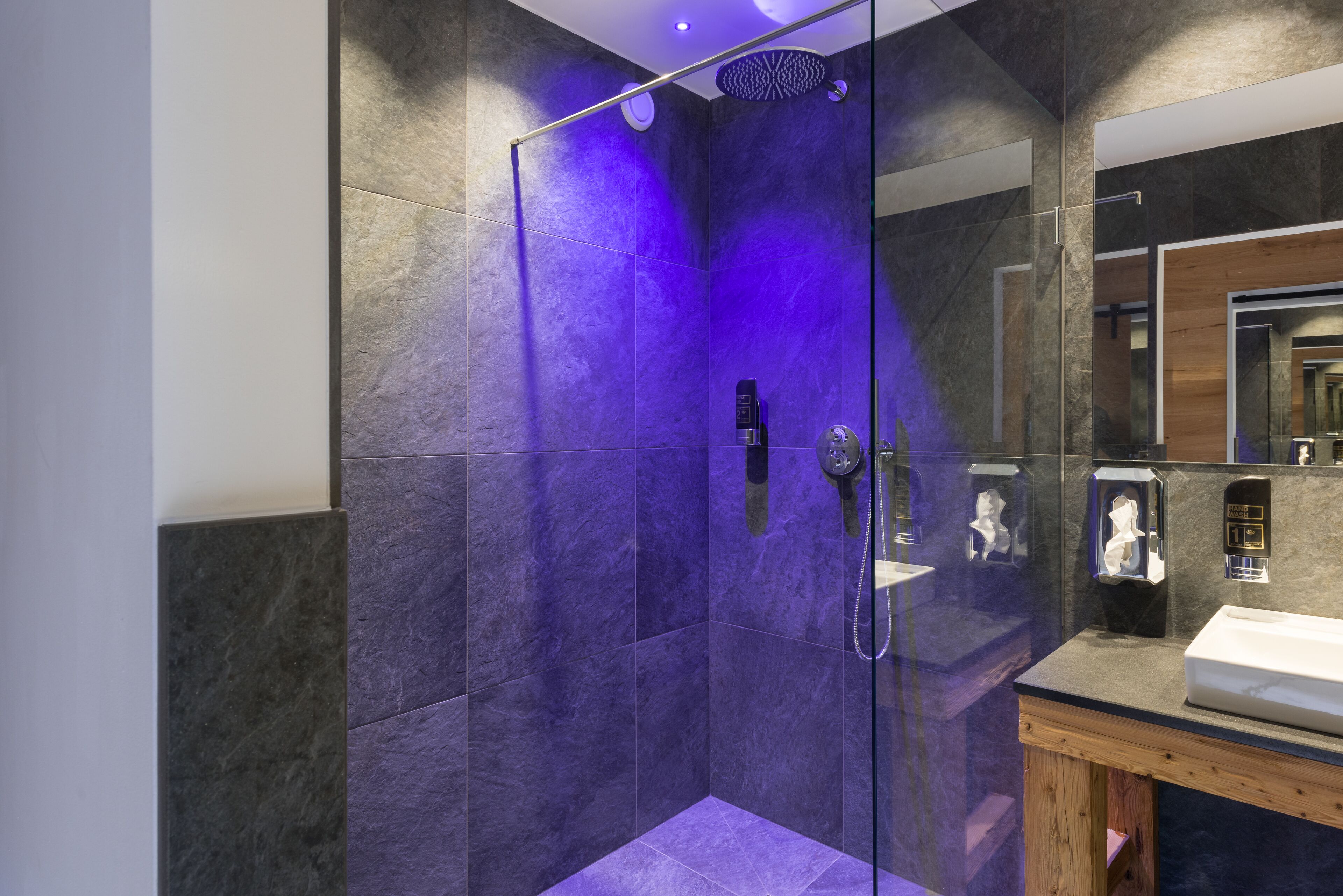 A modern bathroom with a glass-enclosed shower, a wooden vanity, and a large mirror.