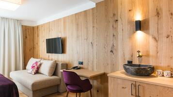 Una camera moderna con parete in legno, una TV a schermo piatto montata sopra una scrivania in legno, un lavandino rotondo in pietra e una sedia viola.