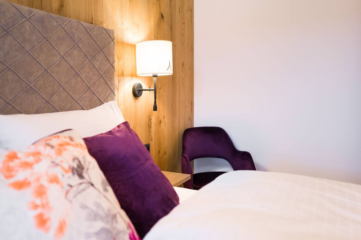 A hotel room with a bed, a nightstand, a lamp, and a chair.