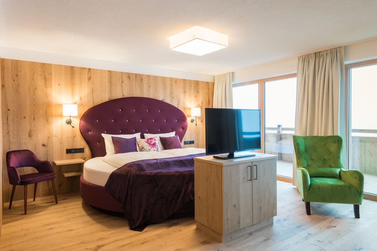 A modern hotel room with a large bed, a television, a green armchair, and a wooden headboard.