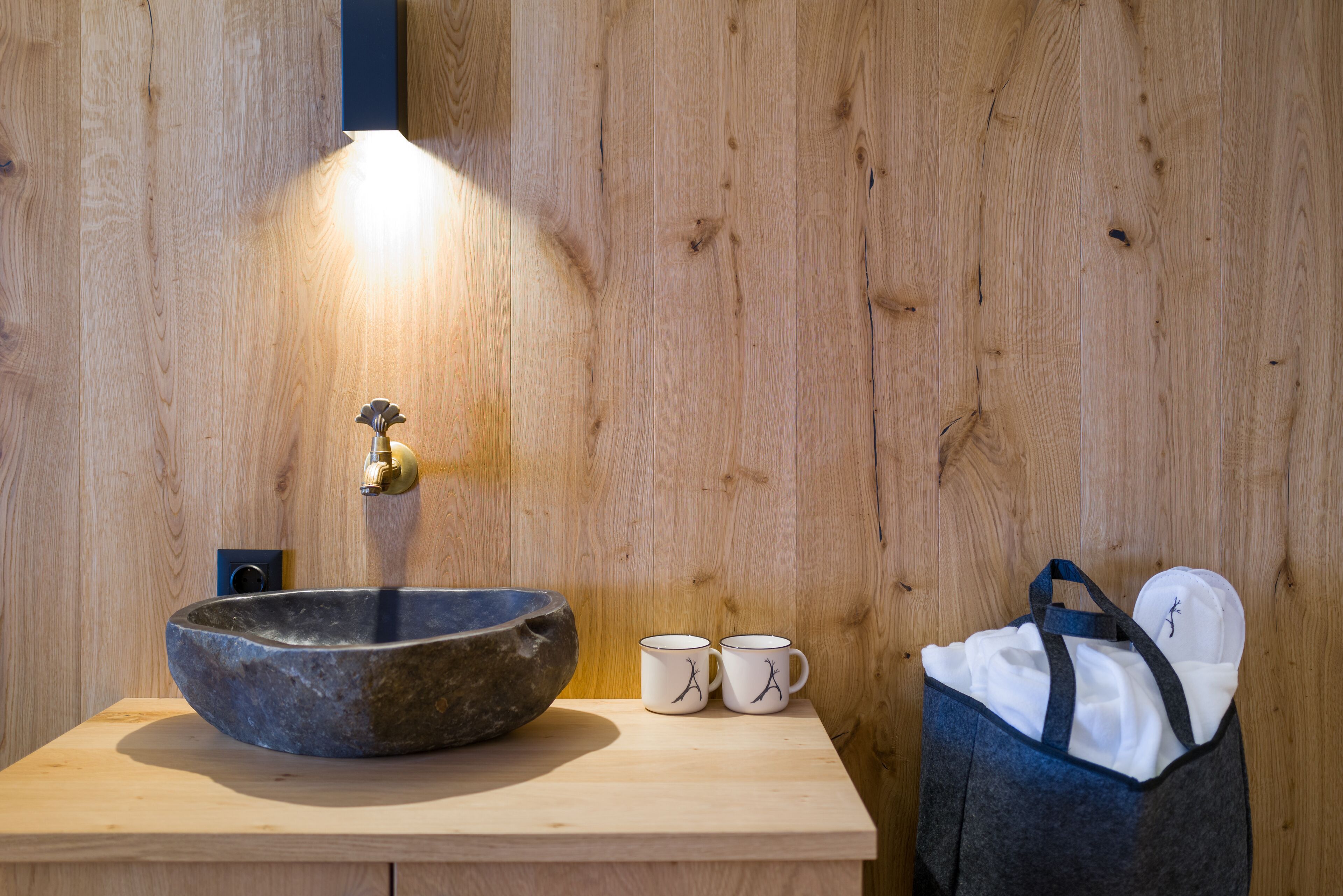 A wooden wall with a stone sink, two white mugs with black designs, and a blue bag.