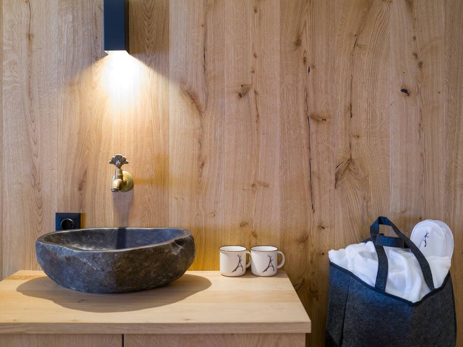 A wooden wall with a stone sink, two white mugs with black designs, and a blue bag.