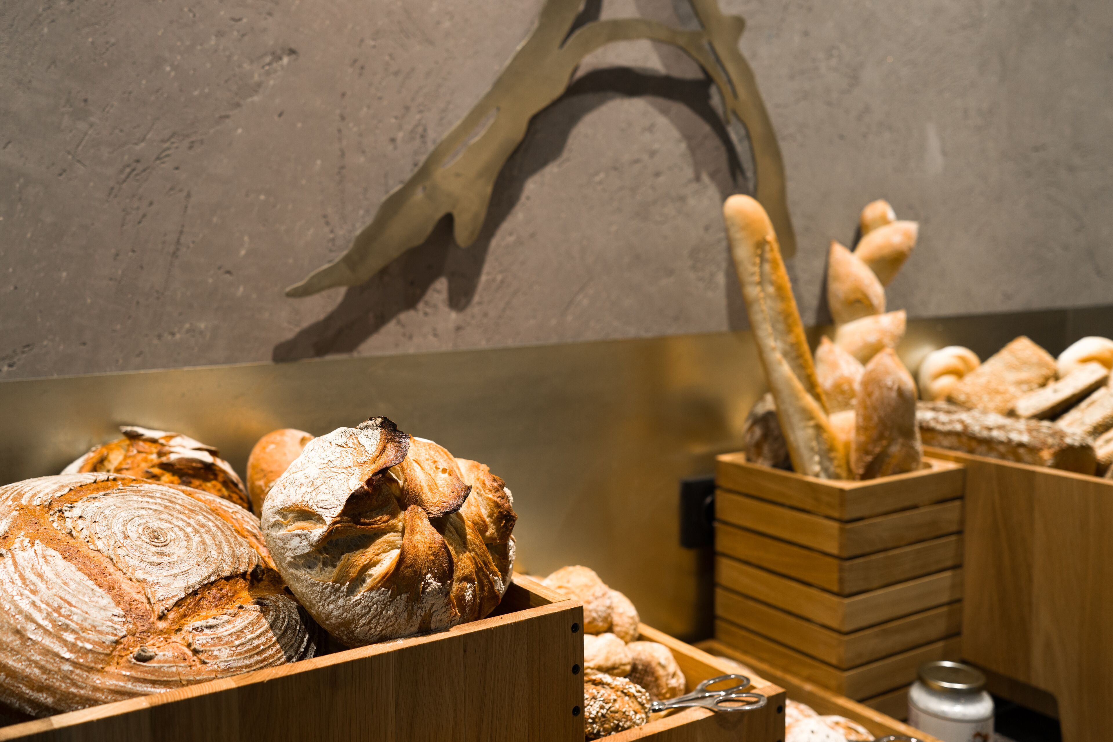 A variety of breads displayed in wooden boxes, with a rustic wall in the background.