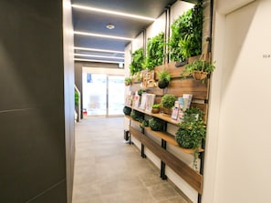 A hallway with a wooden bench, potted plants, and a wall-mounted shelf with magazines and books.