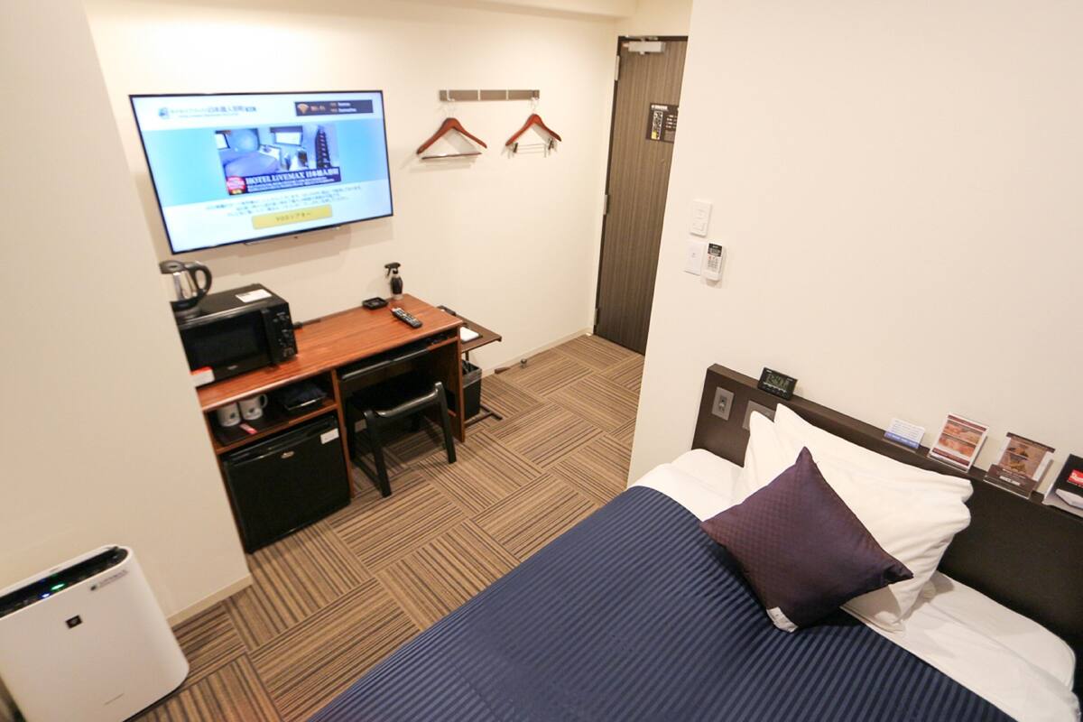 Een hotelkamer met een bed, een bureau met een computer, een aan de muur bevestigde televisie en een kleine prullenbak.