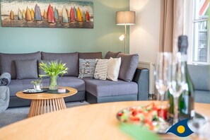 Een moderne woonkamer met een grijze bank, een houten salontafel en een schilderij van zeilboten aan de muur.
