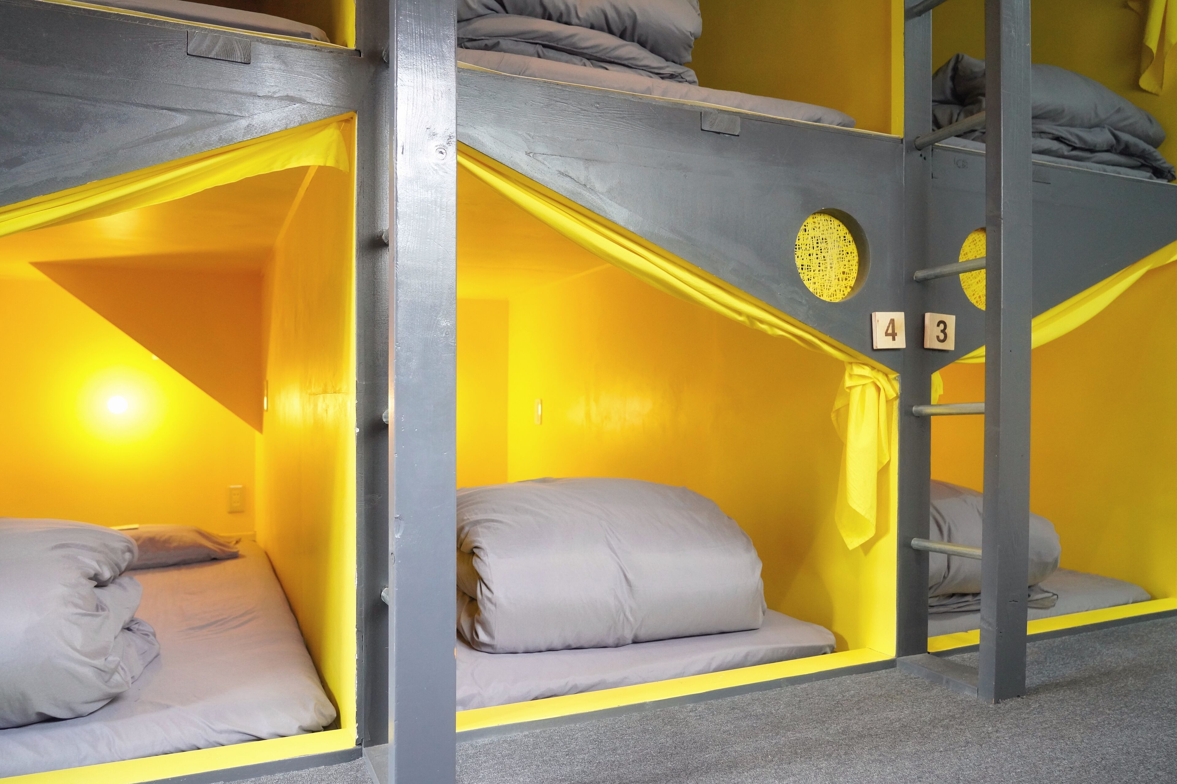 A bunk bed room with a yellow interior, grey bedding, and a ladder.