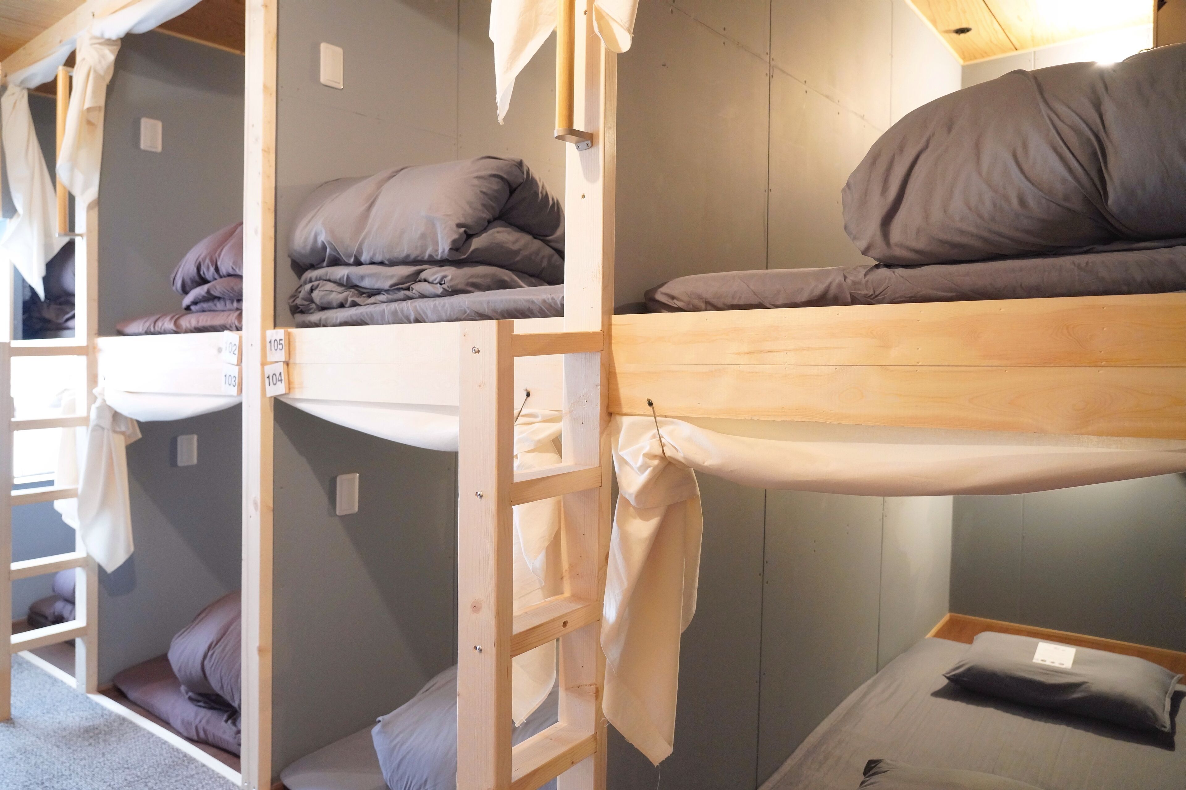 A bunk bed room with wooden frames, grey bedding, and a ladder.