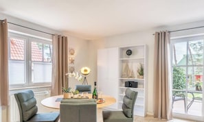 A room with a round table, two chairs, a bookshelf, and a window with curtains. - Miss Loddin's Apartment at Willi's (includes beach chair) - + Miss Loddin at Willi's (Loddin)