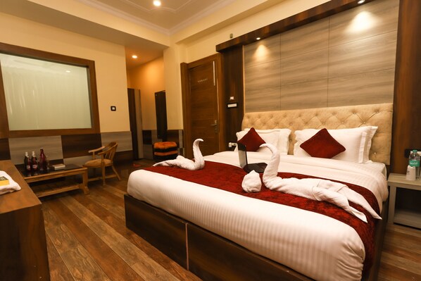 A hotel room with a large bed, a TV, a wooden desk, and a comfortable chair. - Hotel The Nest (Dharamshala)