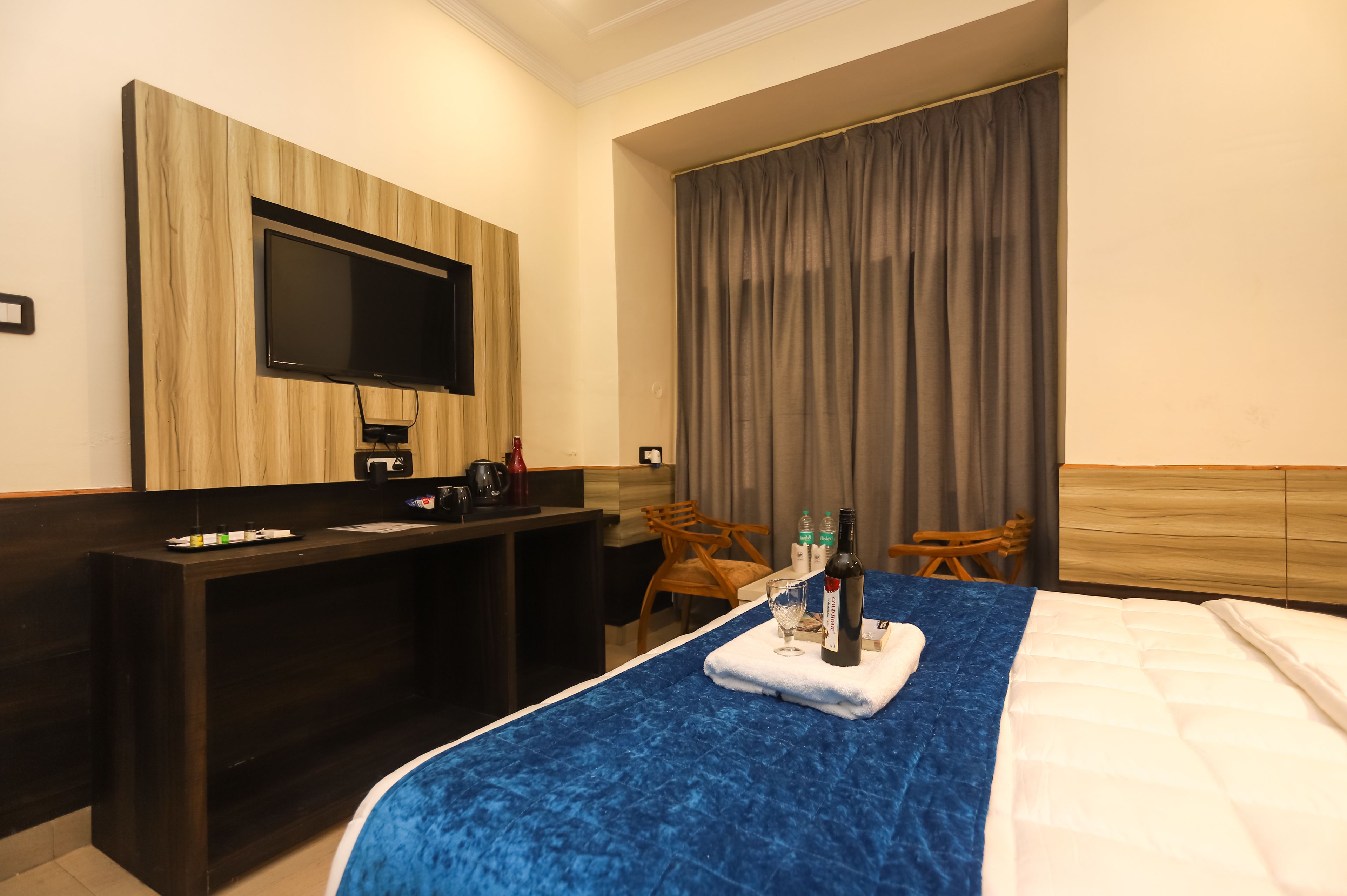 Ein Hotelzimmer mit Bett, Wandfernseher, Schreibtisch mit Kaffeemaschine und einem Vorhangfenster.