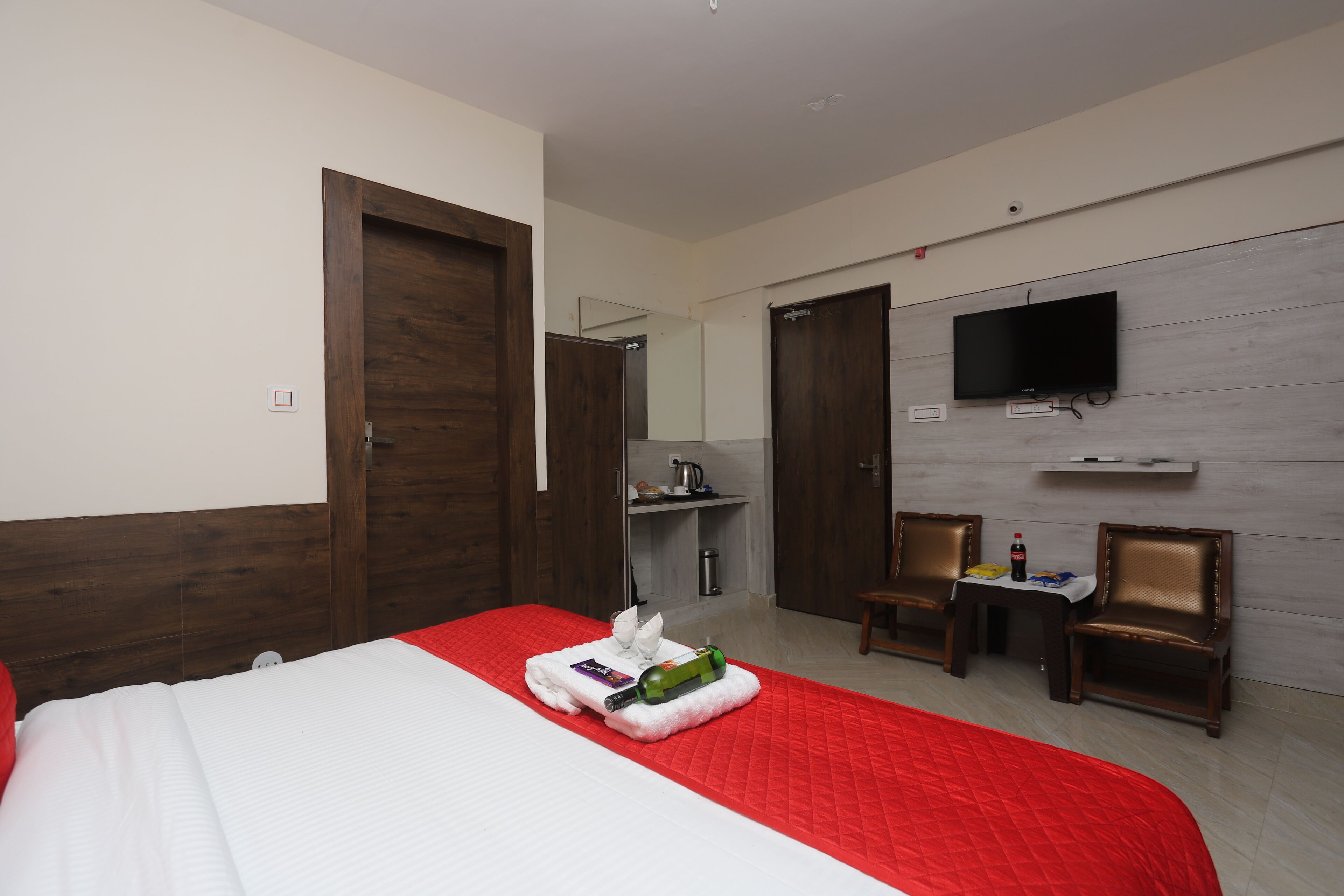 A hotel room with a bed, a TV mounted on the wall, a small table with chairs, and a kitchenette area.