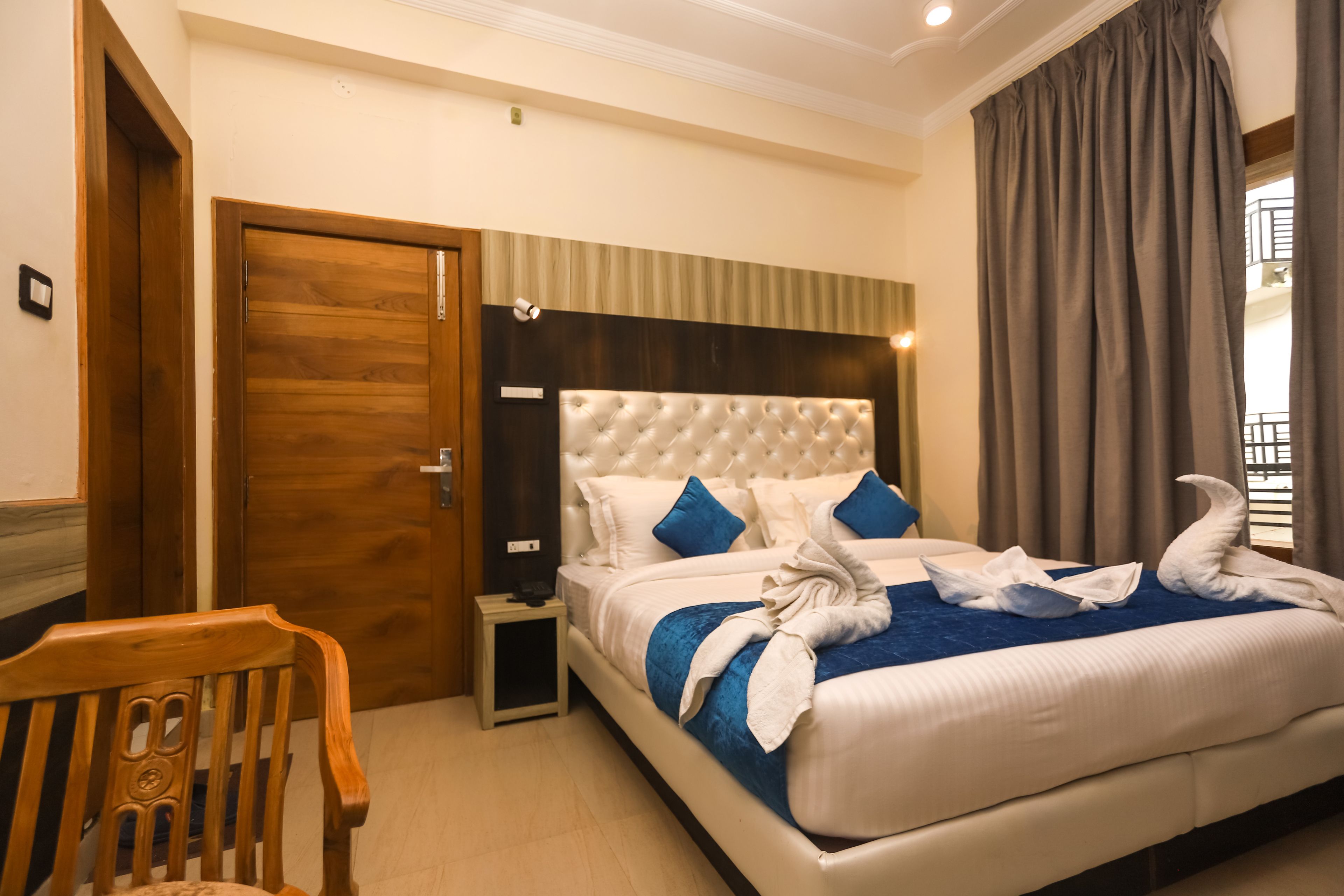 A hotel room with a large bed, a wooden chair, a nightstand, and a door.