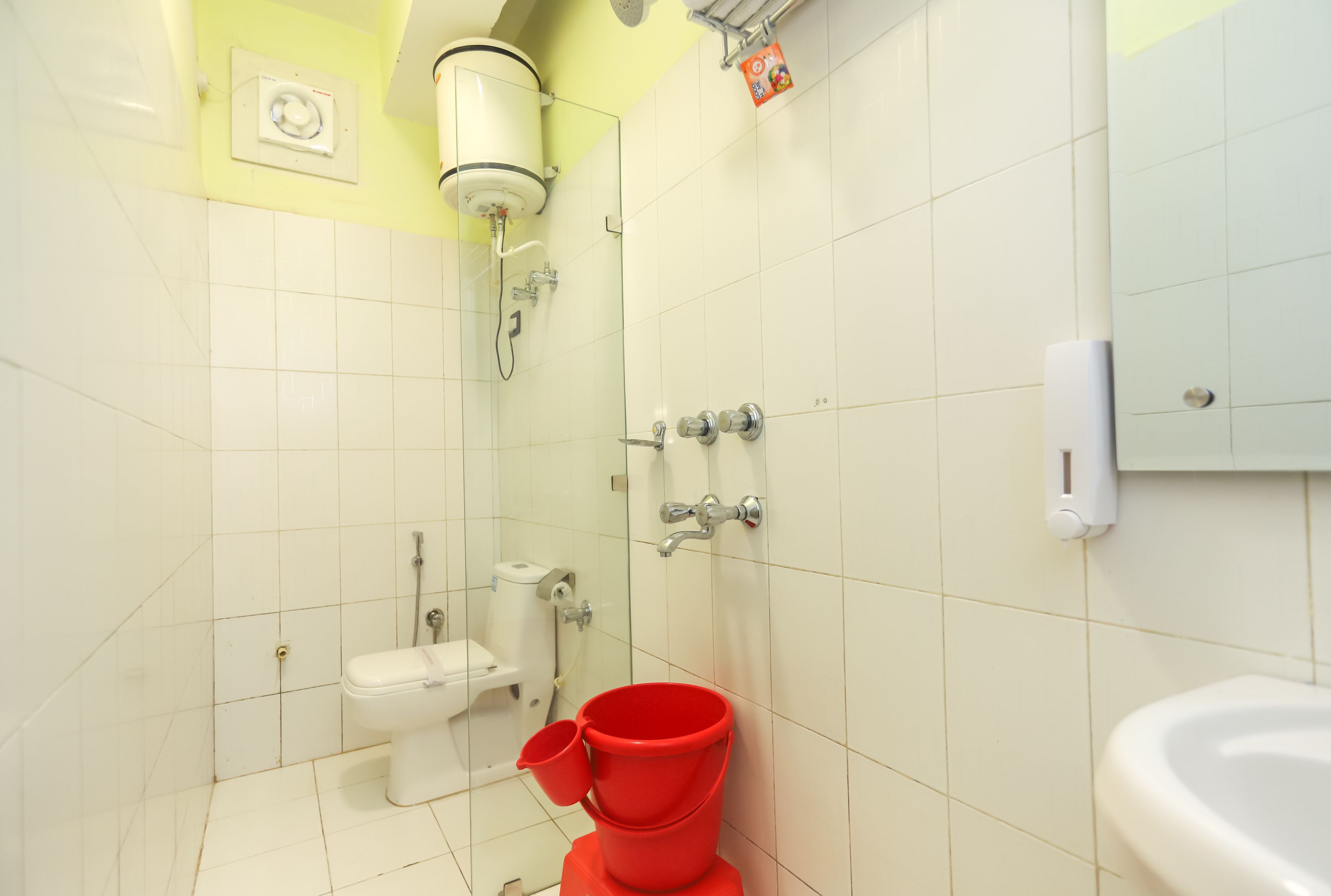 A bathroom with white tiles, a toilet, a bidet, a shower, and a red bucket.