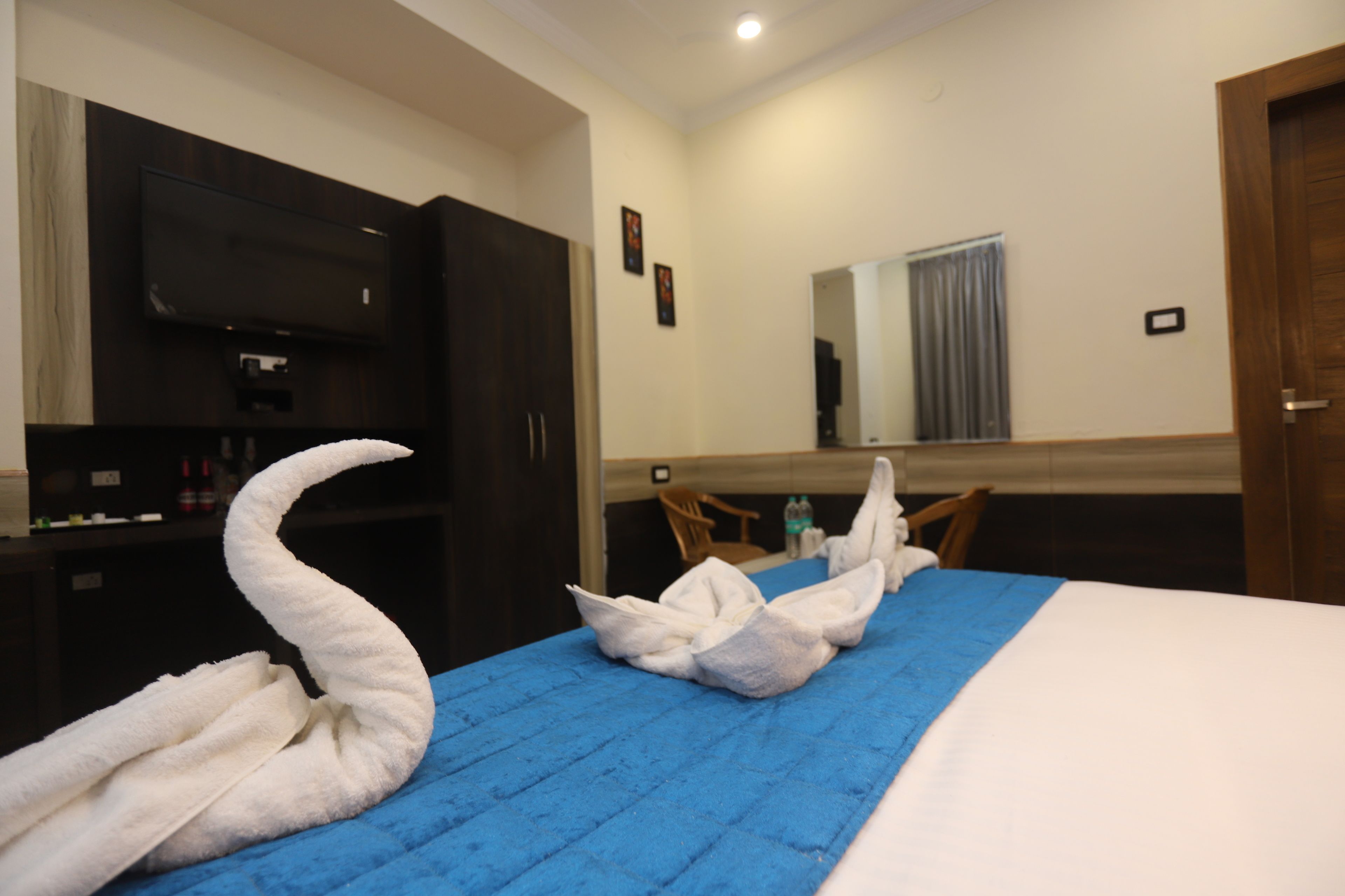 A hotel room with a bed, a TV, a mirror, and a blue bedspread.