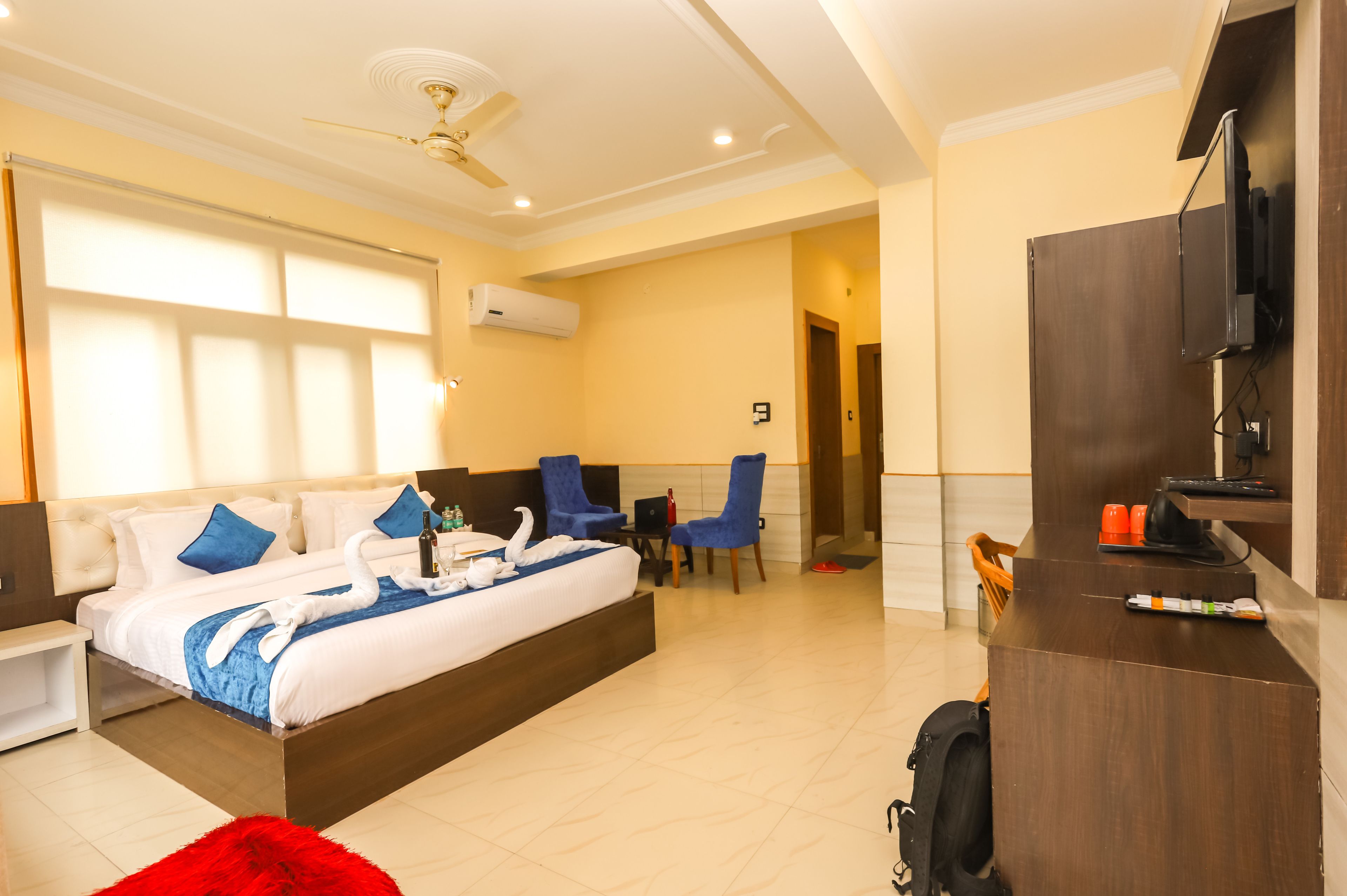 A hotel room with a large bed, a desk, a chair, a TV, and a ceiling fan.
