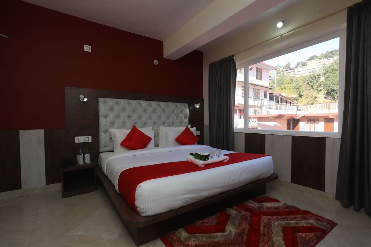 A hotel room with a large bed, a view of buildings through the window, and a red and white color scheme.