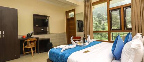 A hotel room with a bed, a desk, a TV, and a window with a view of greenery.