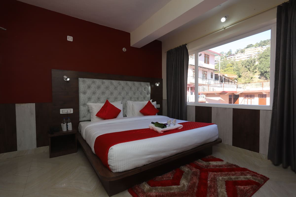 A hotel room with a large bed, a view of buildings, and a red and white color scheme.