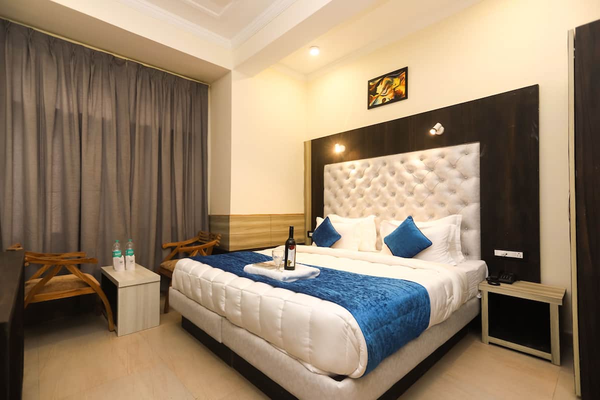 A hotel room with a large bed, a wooden nightstand, a small table with two bottles, and a chair.