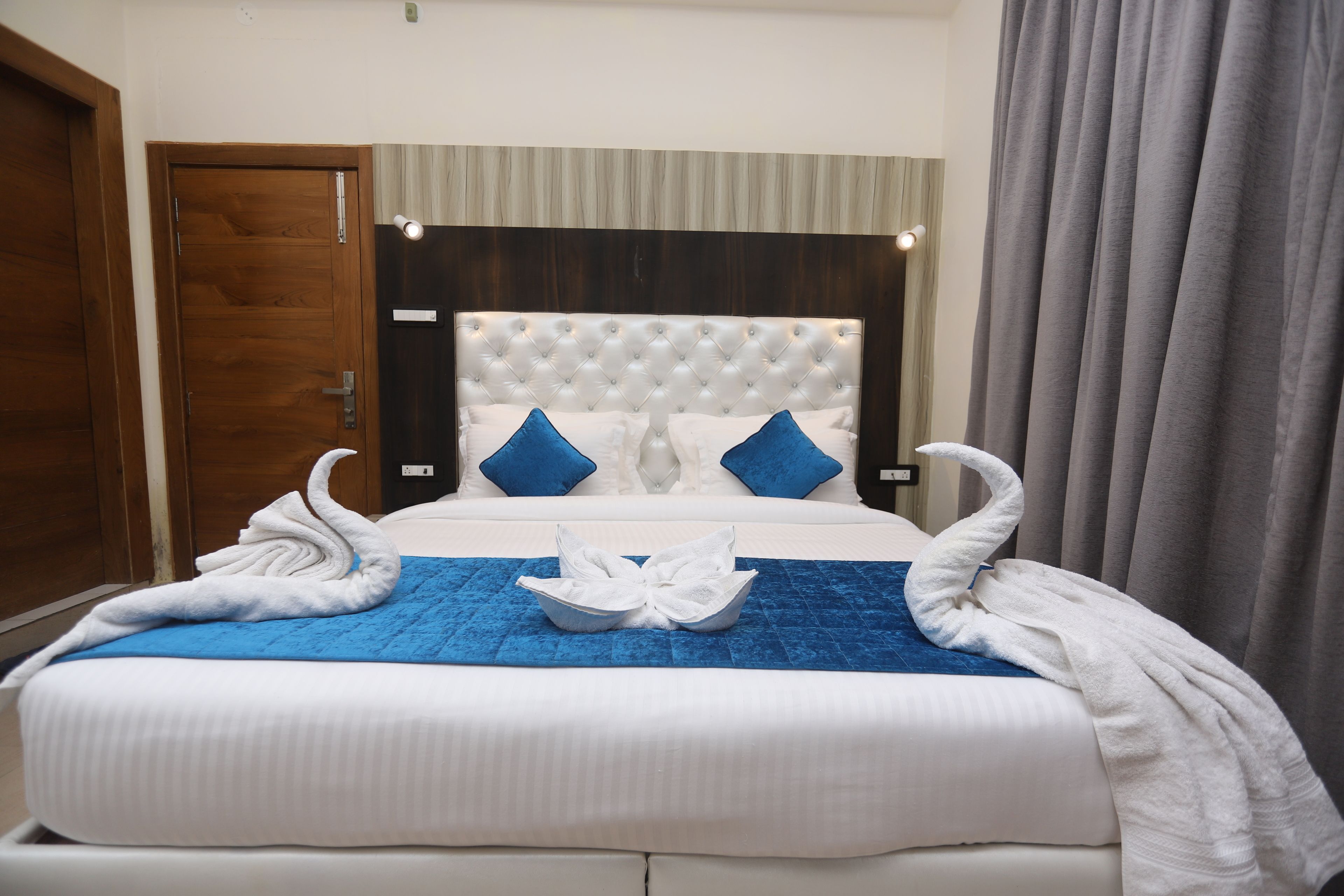 A neatly made bed with a blue blanket, two pillows, and two towels arranged in a swan shape.