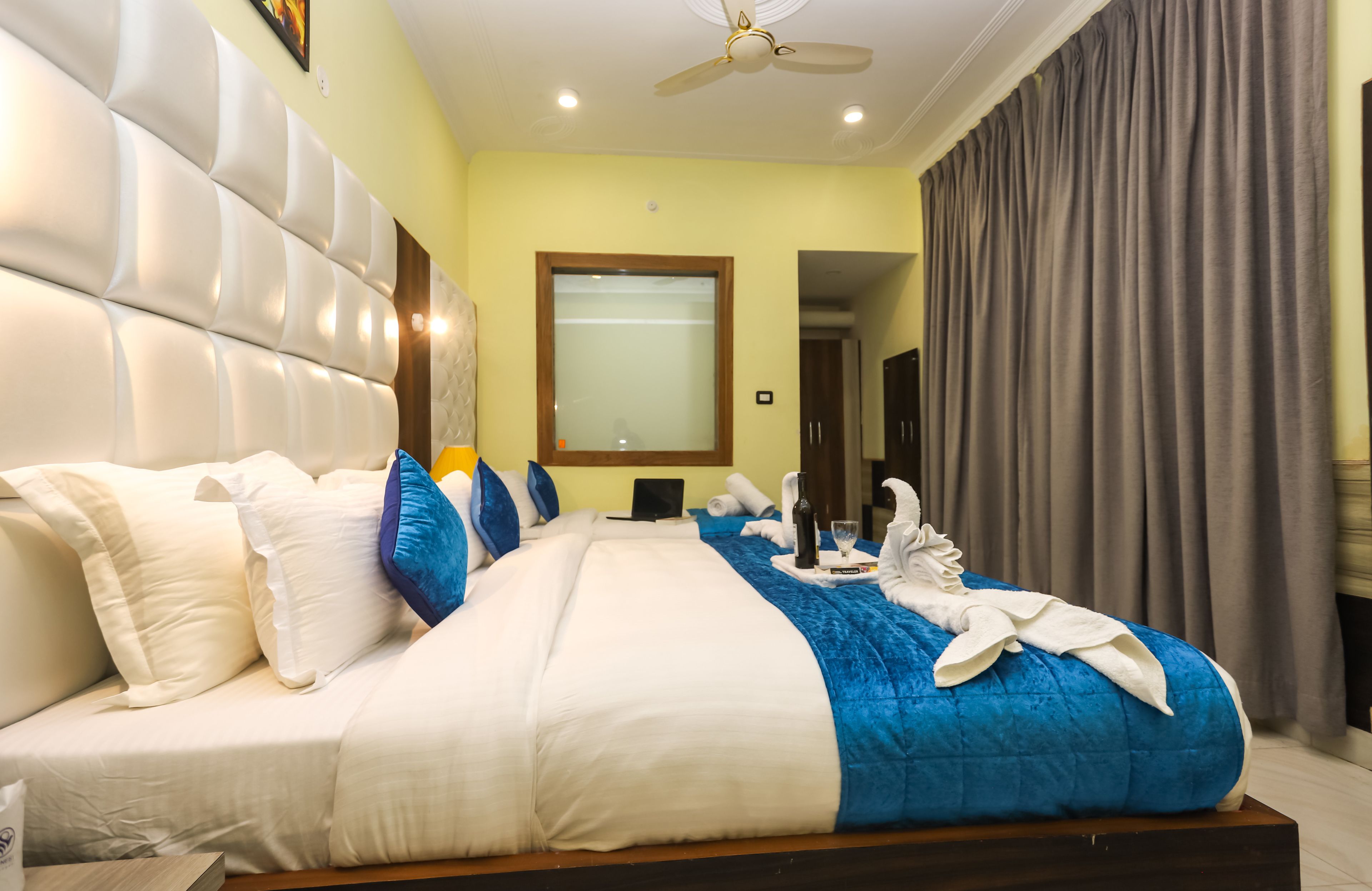 A hotel room with a large bed, a ceiling fan, a window with curtains, and a door leading to another room.
