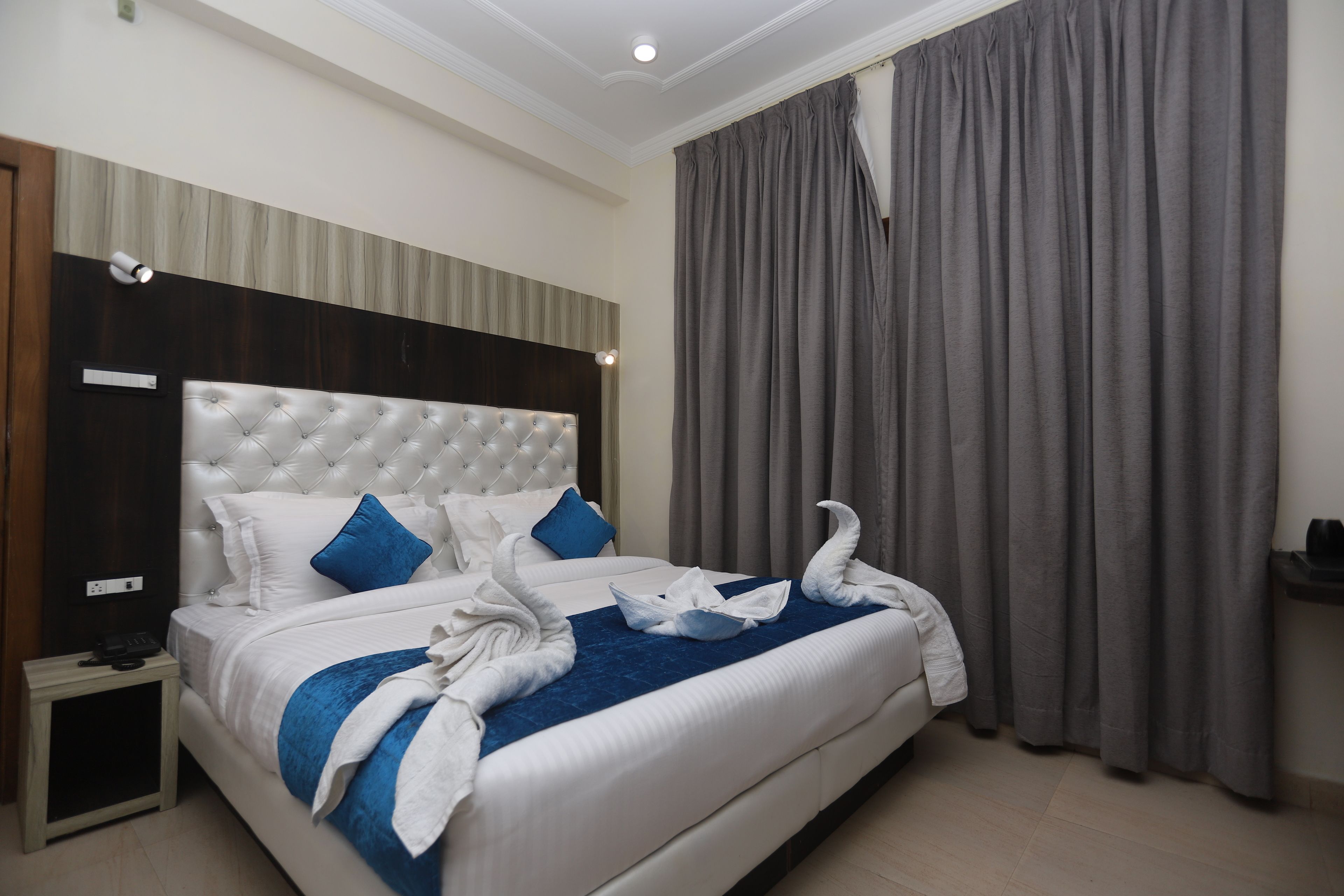 A hotel room with a large bed, a headboard, a bedside table, and a curtain.