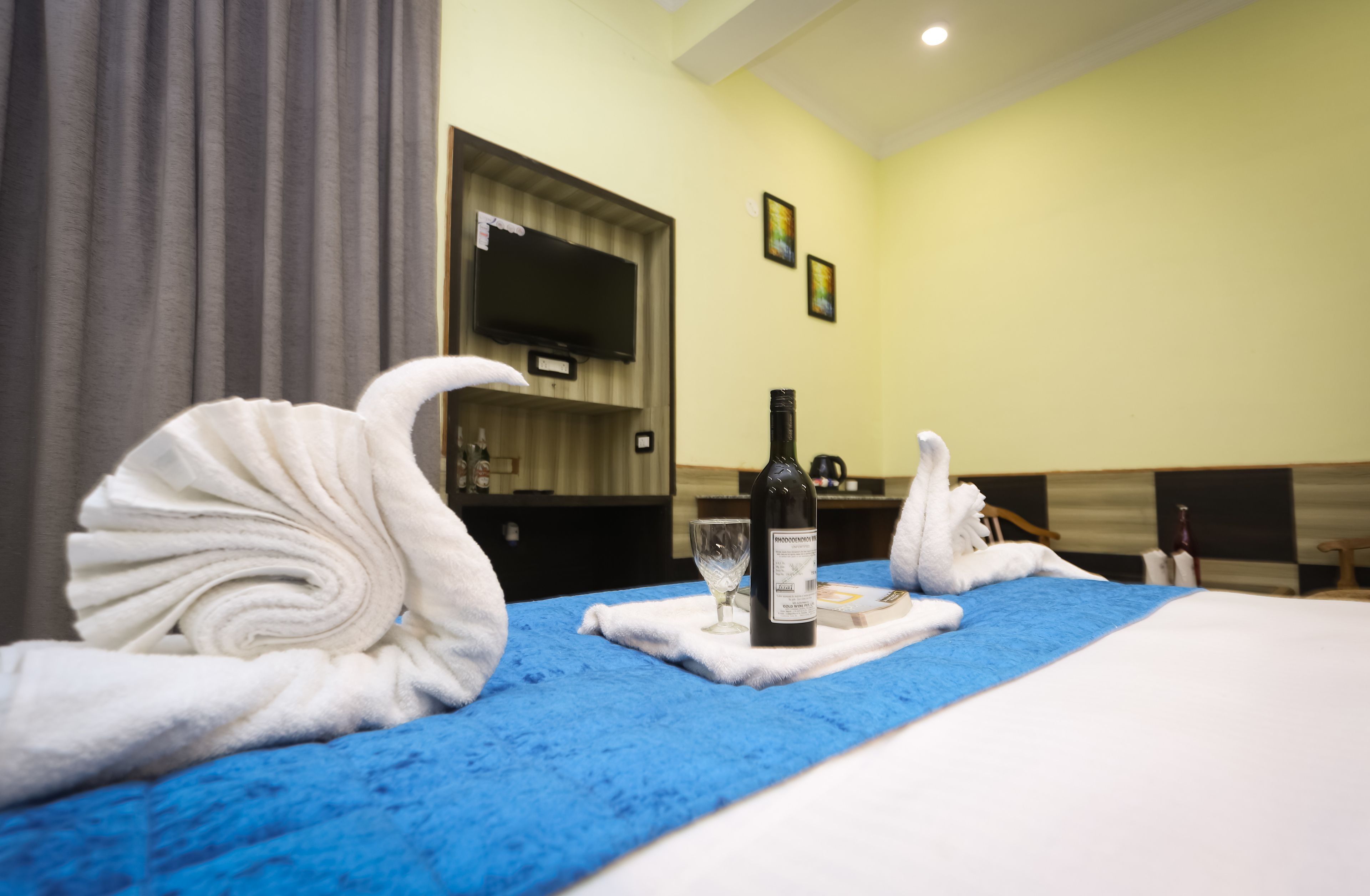 A hotel room with a bed, a TV mounted on the wall, and a bottle of wine on the bed.