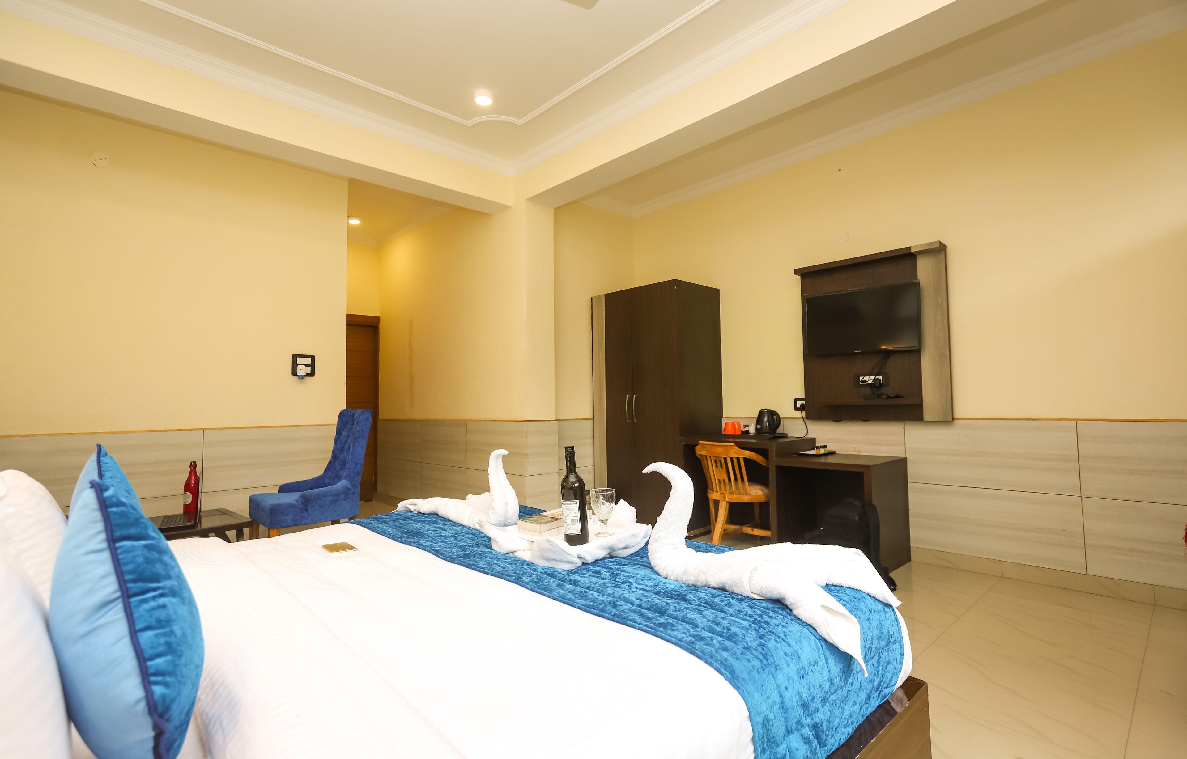 Quarto de hotel com cama, escrivaninha, televisão e uma cadeira.