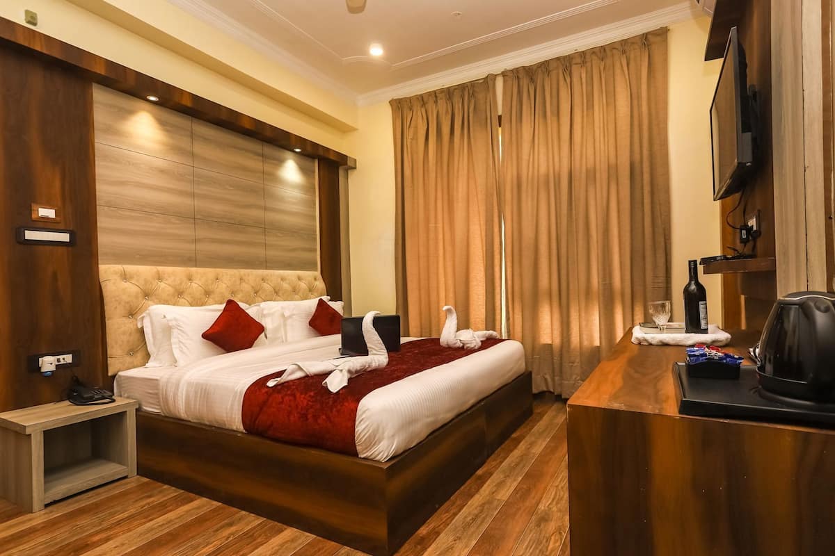 A hotel room with a large bed, a desk with a kettle, a television, and a minibar.