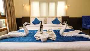 A hotel room with a large bed, a blue quilt, two towels shaped like swans, a bottle, and a book. - Hotel The Nest (Dharamshala)