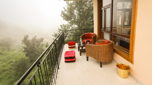 A balcony with wicker furniture, a red cushion, and a wicker basket. - Hotel The Nest (Dharamshala)