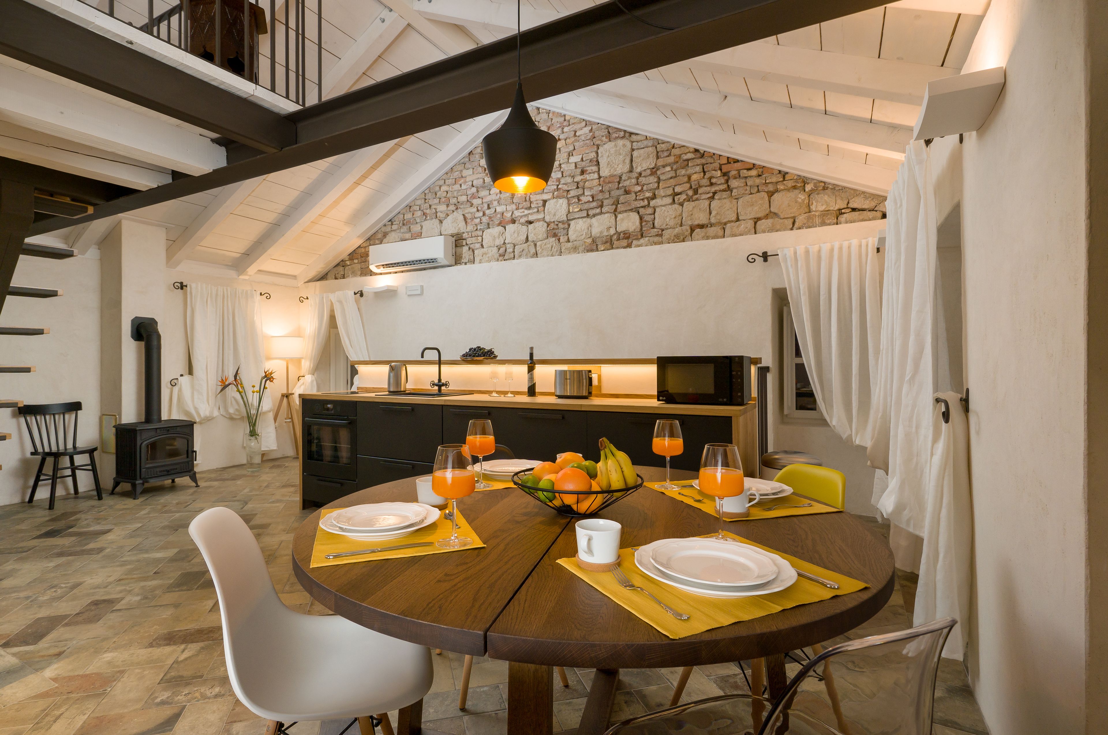 Un comedor con una mesa redonda dispuesta para cuatro, una pared de piedra y una cocina al fondo.