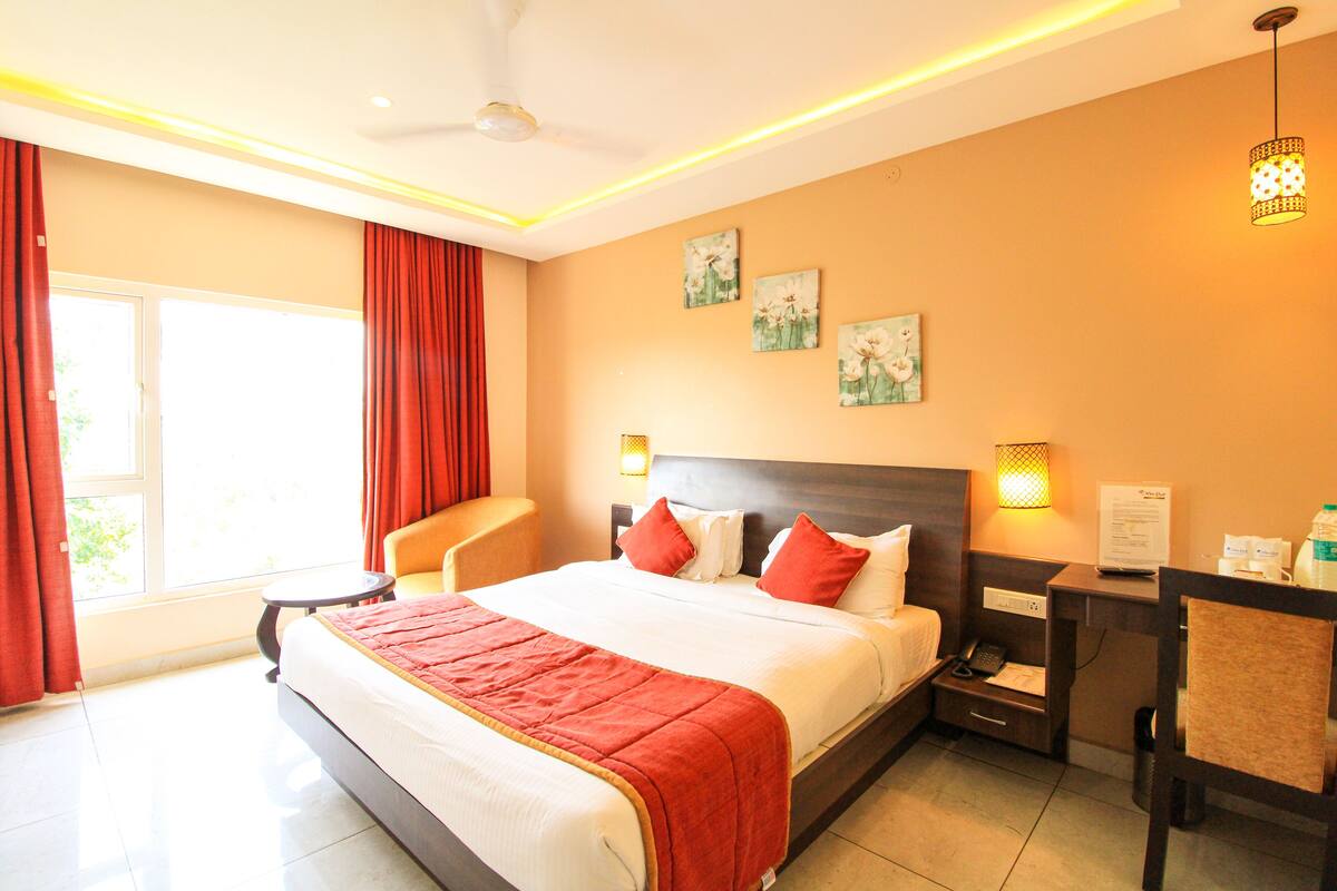 A hotel room with a large bed, a desk, a chair, and a window with curtains.