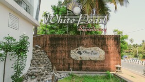 Een bordje voor White Pearl Residences, met een stenen muur en een palmboom op de achtergrond.