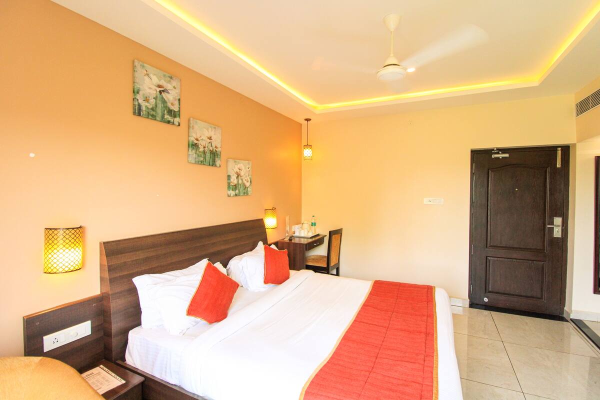 A hotel room with a large bed, a desk, a chair, and a door.