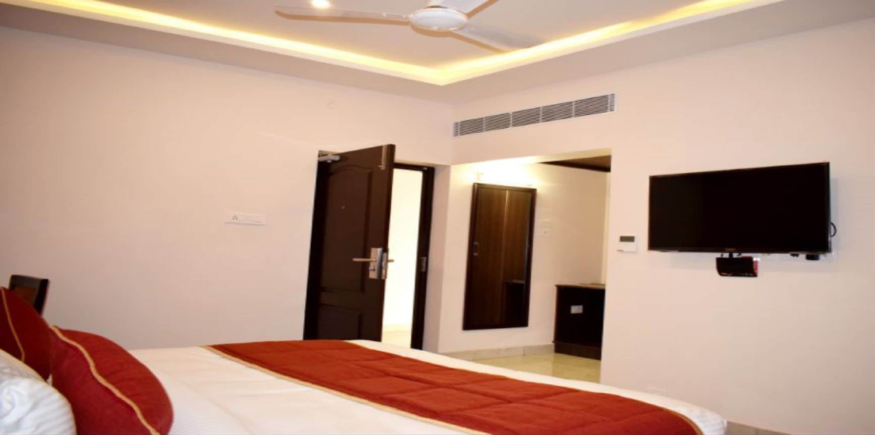 A hotel room with a bed, a ceiling fan, a TV mounted on the wall, and a door leading to another room.