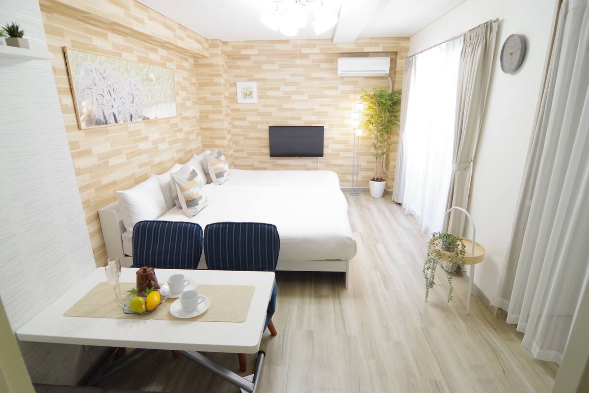 A modern hotel room with a bed, a TV, a dining table with breakfast items, and a potted plant.
