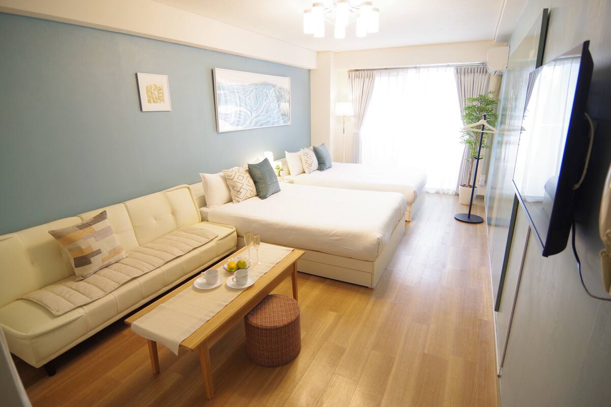 A modern hotel room with a sofa, a bed, a flat-screen TV, and a dining table with a placemat.