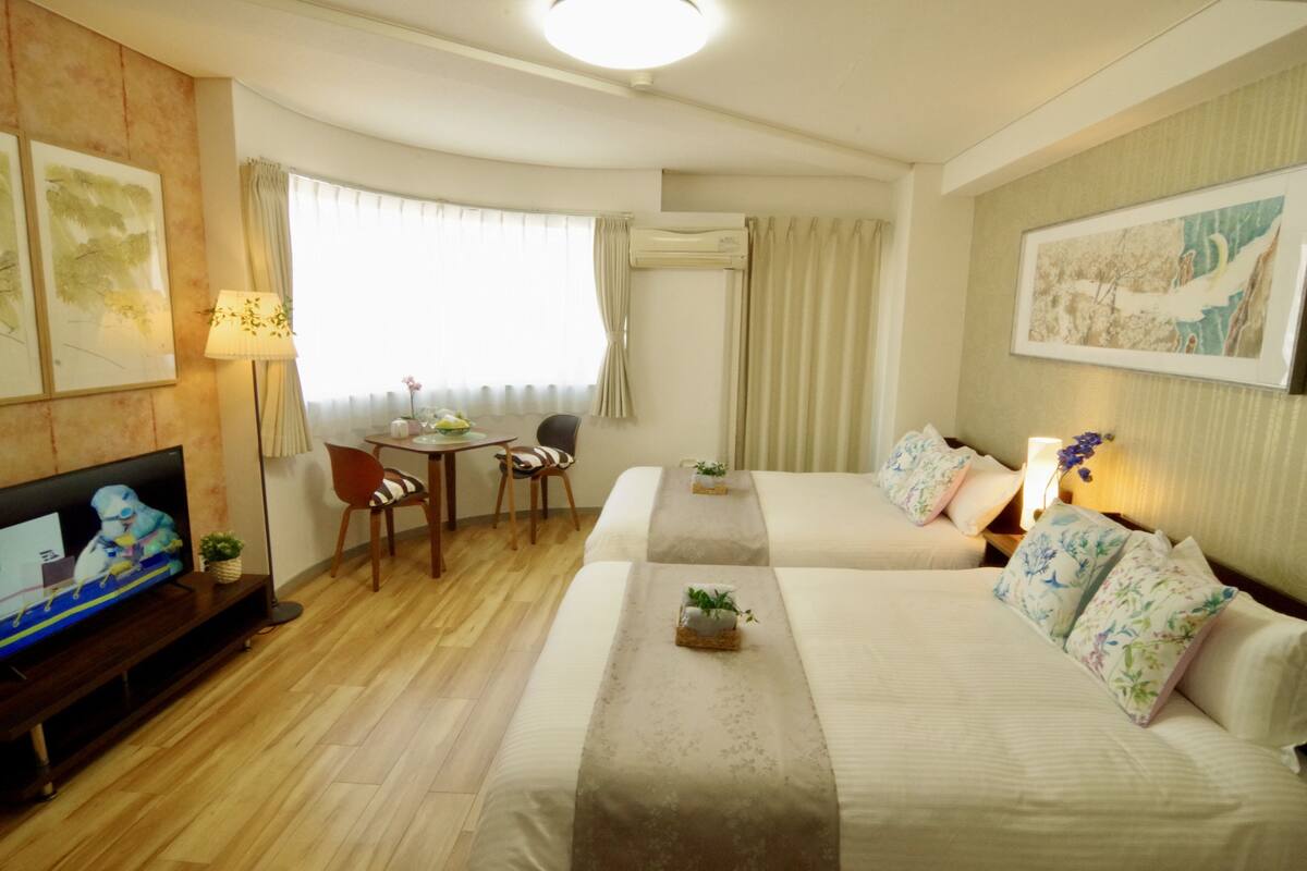A hotel room with two beds, a TV, a desk, and a chair.